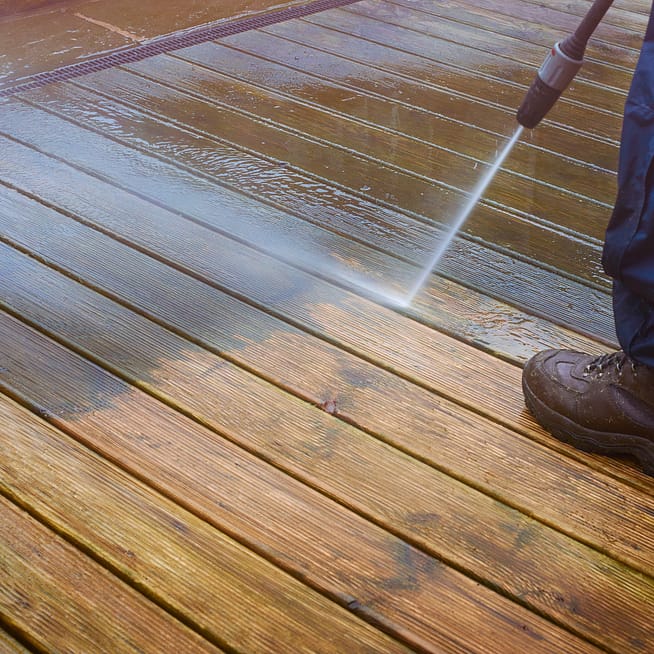 A pressurized jet of water removes grime from wooden boards.